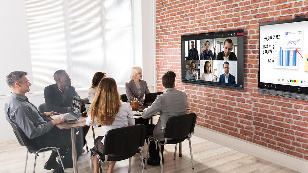 Meeting room equipped with two SMART boards, one for video conferencing and another for digital collaboration, facilitating a hybrid work environment.
