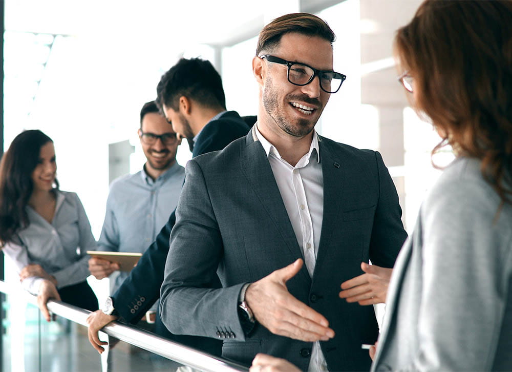 Group of professionals conversing and smiling during a casual meeting in a modern office environment.
