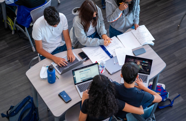Group of students working on laptops and assignments during a study session.