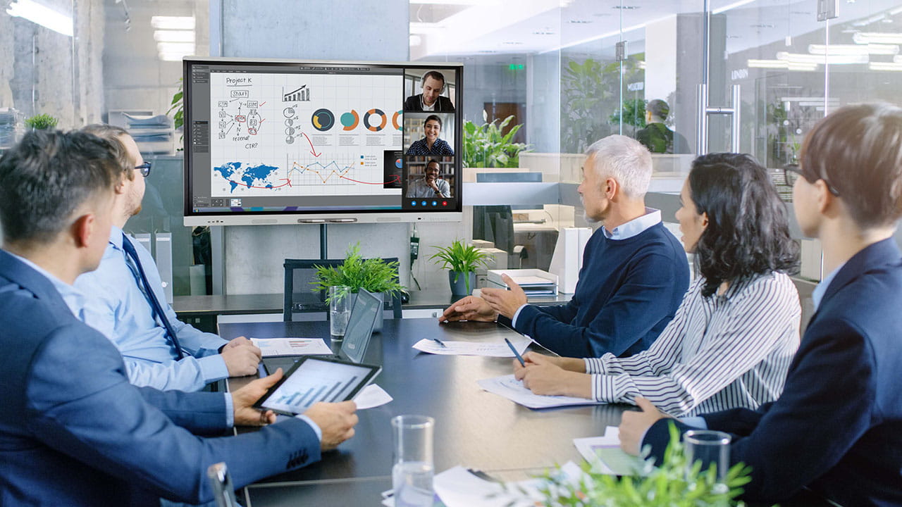 A corporate meeting room with executives discussing data visualizations displayed on a SMART Board.